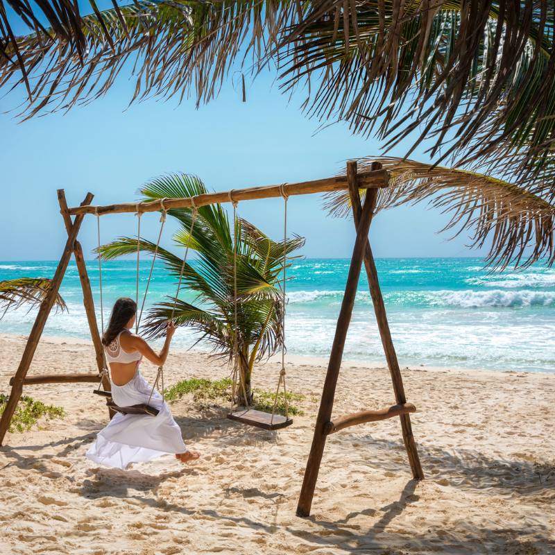 A Tulum, Mexico vacation with girl on swing at the beach with blue water