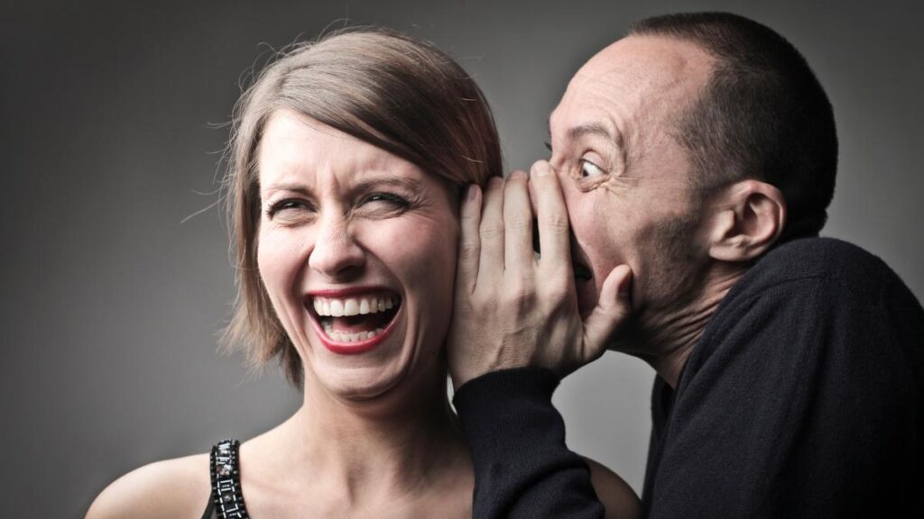 man whispering to woman laughing