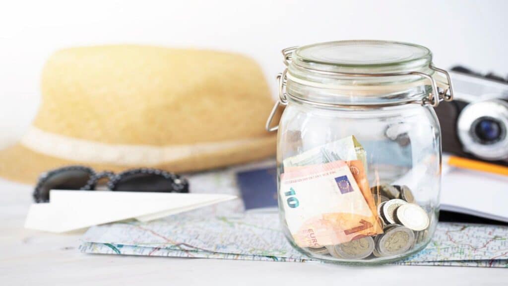Close up of glass jar filled with money on open map. Vacation, travel concept