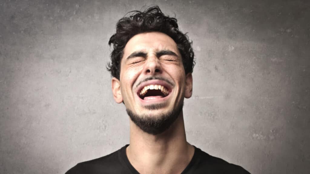 man laughing eyes closed gray background - OllyyShutterstock
