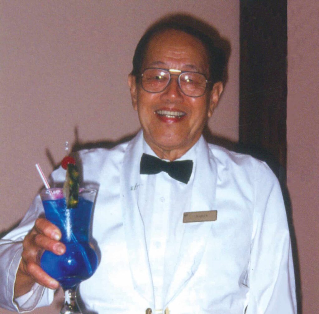 Henry Lee in a white tuxedo holding a Blue Hawaiian cocktail drink
