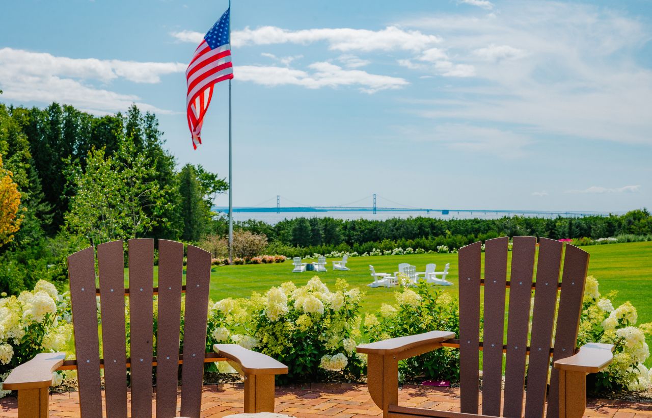 two adirondack chairs on a green lawn with an American flag in the yard
